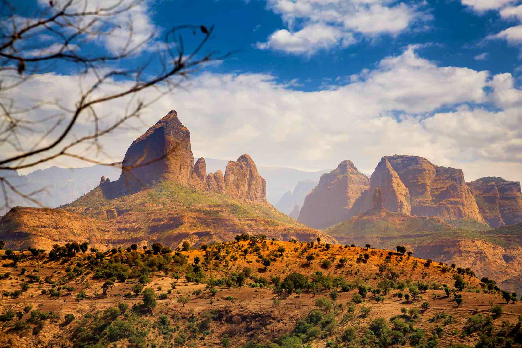 Dramatic rocky mountain peaks rising above arid Ethiopian landscape with scattered vegetation and blue sky with white clouds